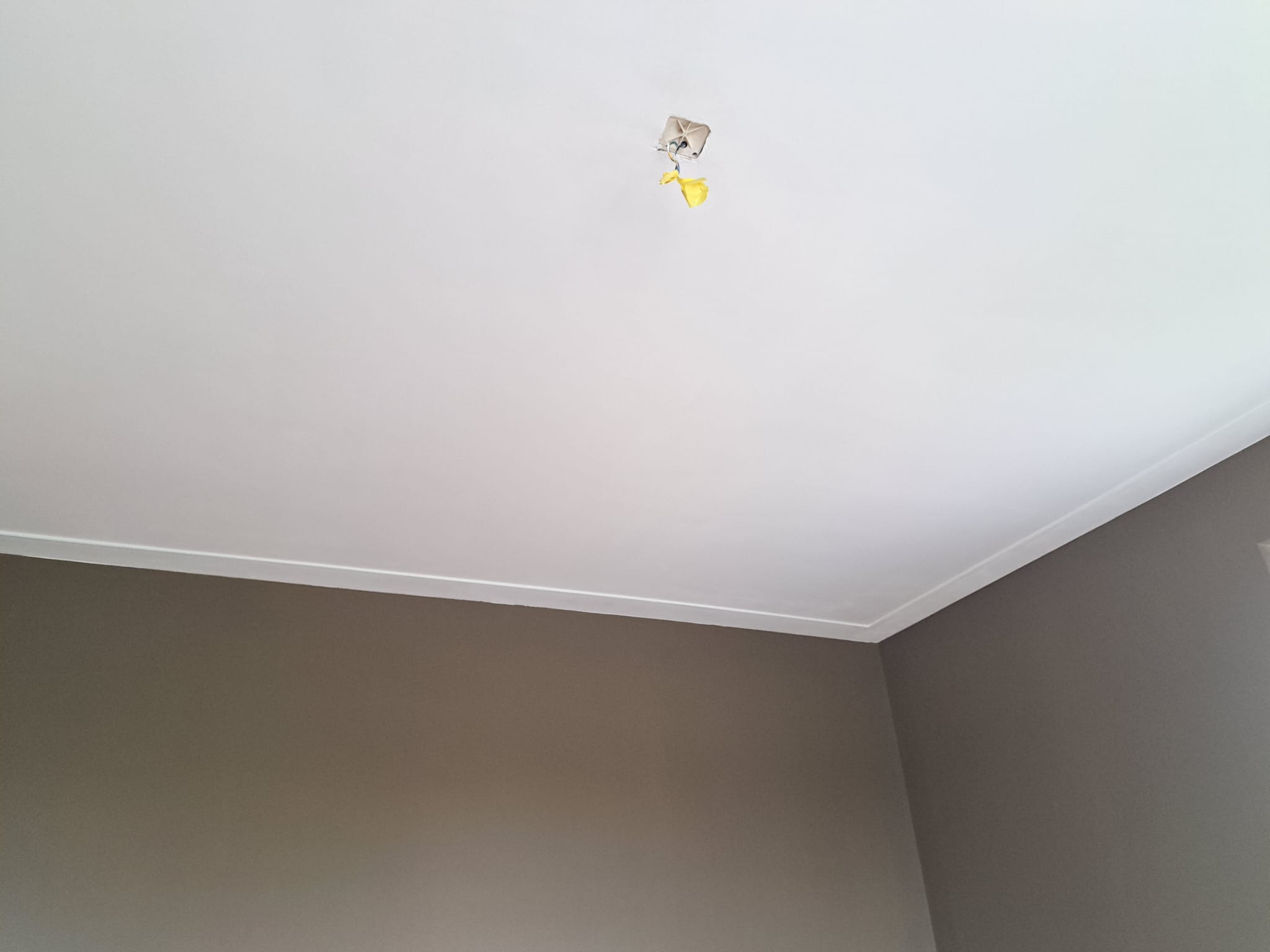Wit gestuct plafond met stucplint langs taupe wanden